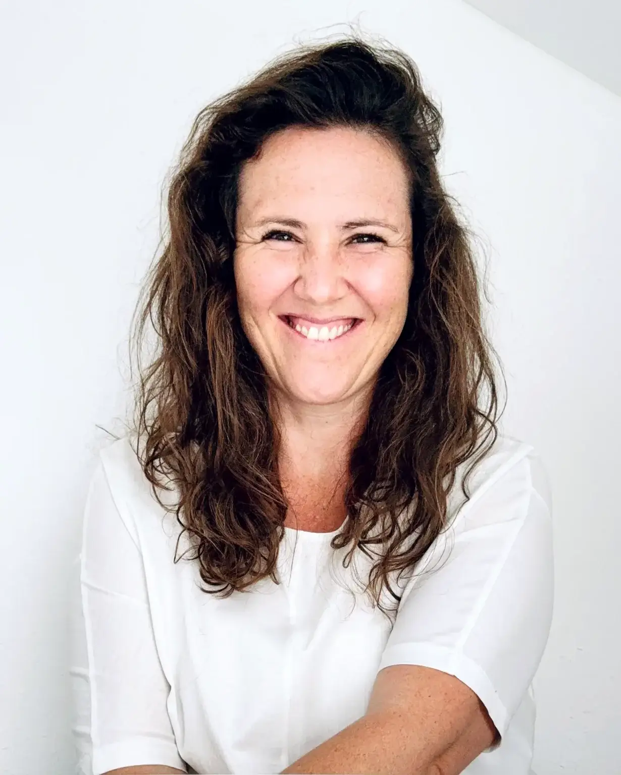 Portrait der Ansprechpartnerin Anita Klein für das Karrierecoaching beim gründungs.center. Sie lacht offen in die Kamera, ihre Haare sind offen. Sie trägt ein weißes Oberteil und sitzt vor einer weißen Wand.