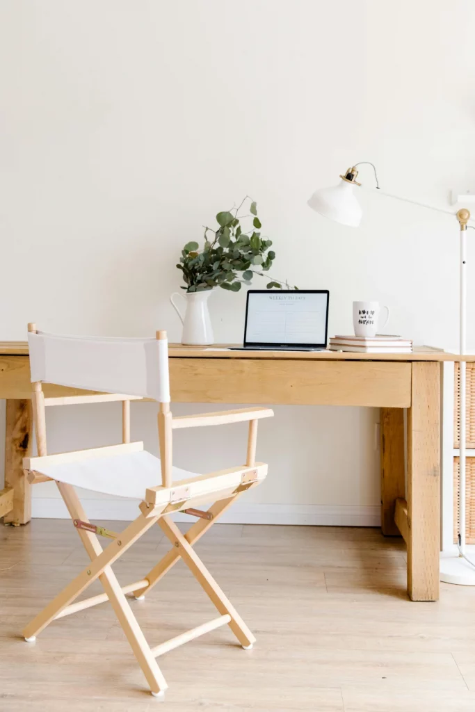 Symbolbild Fragen zum Bildungsgutschein: Ein helles Büro, mit einem Schreibtsich aus Holz, auf dem ein Laptop aufgeklappt steht. Vor dem Schreibtisch steht ein Regiestuhl in weiß.